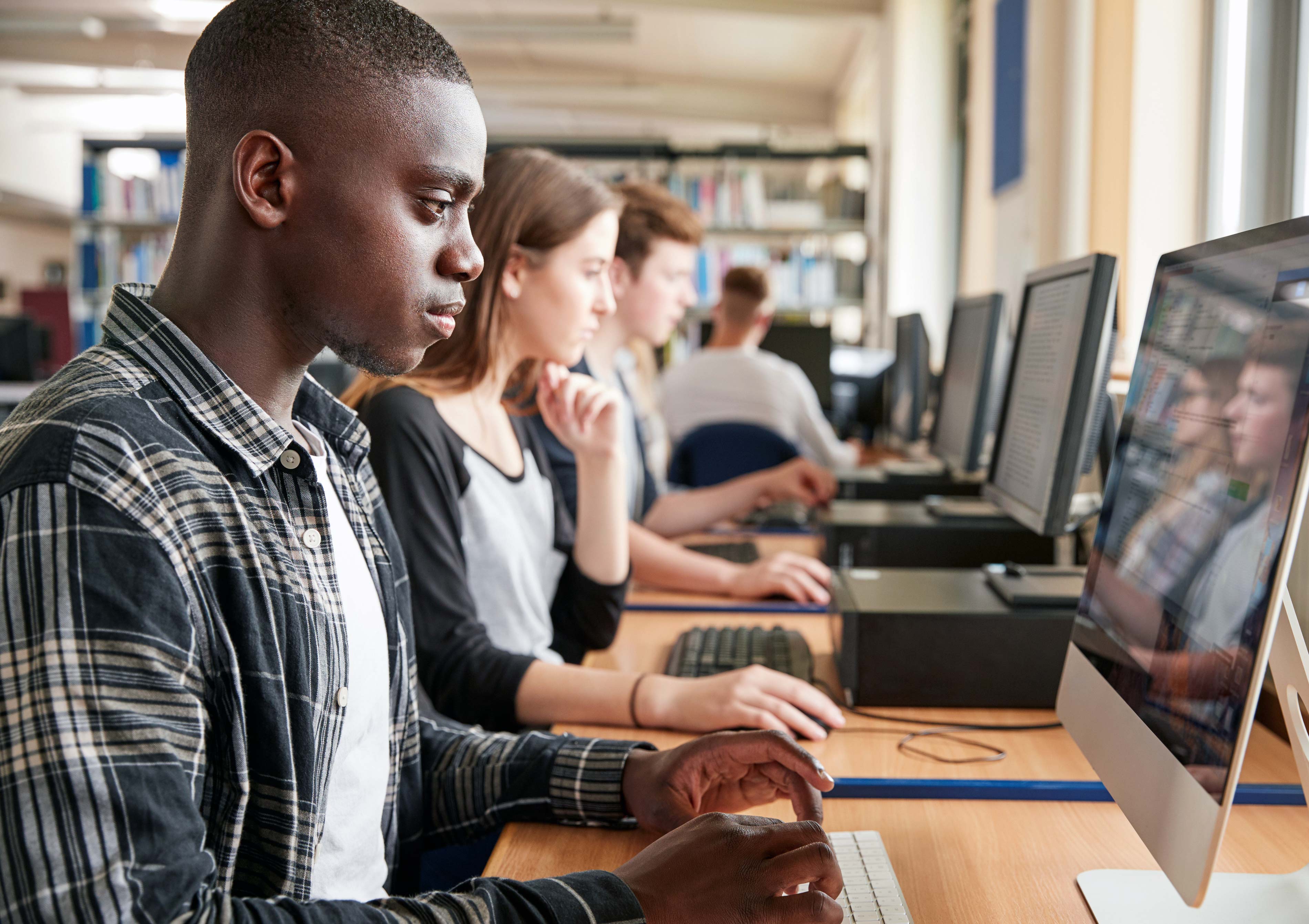 College students working on desktop computers in a library or classroom setting.
