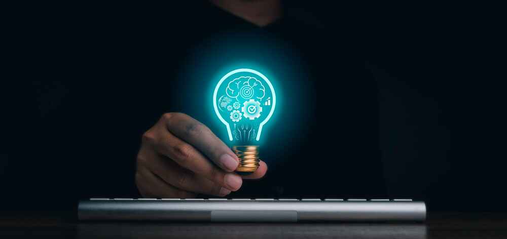 Photo of a man holding a light bulb over a keyboard, with graphics inside the light bulb such as gears and a brain
