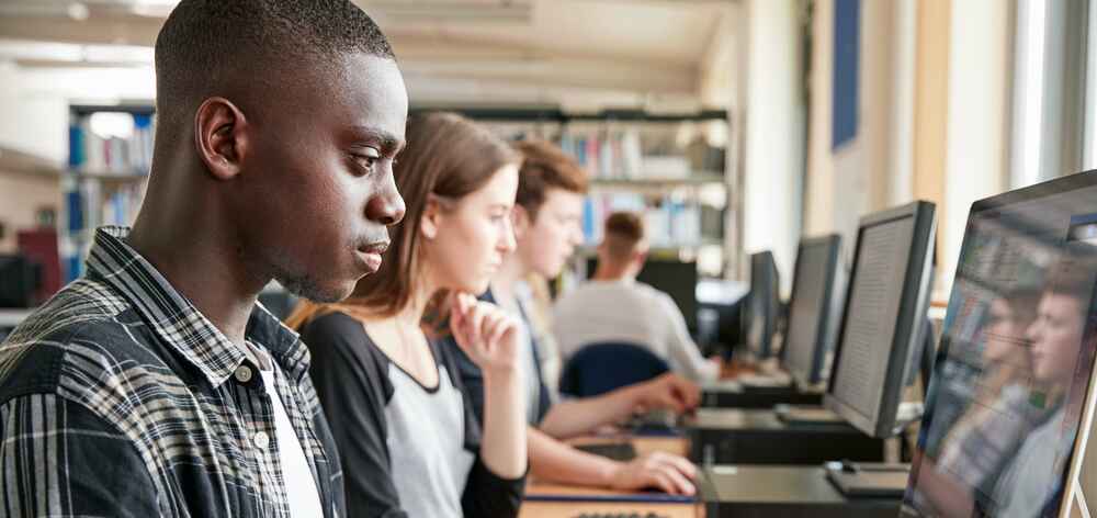 College students working on desktop computers in a library or classroom setting.