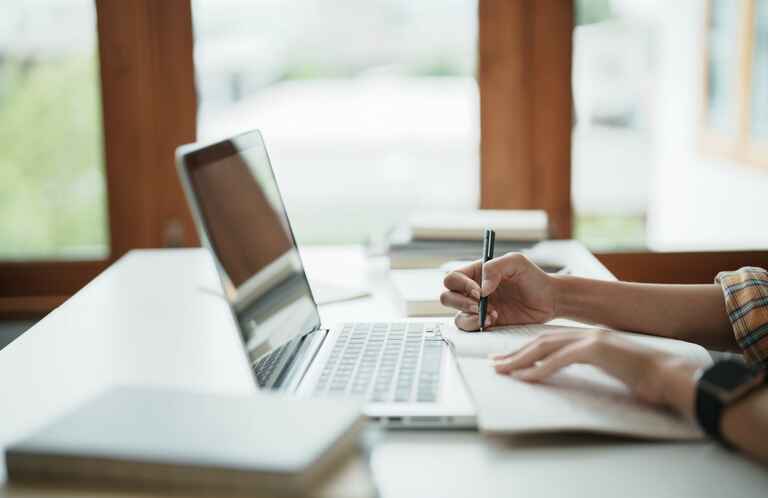 Young woman student busy studying make notes in notebook and using laptop.