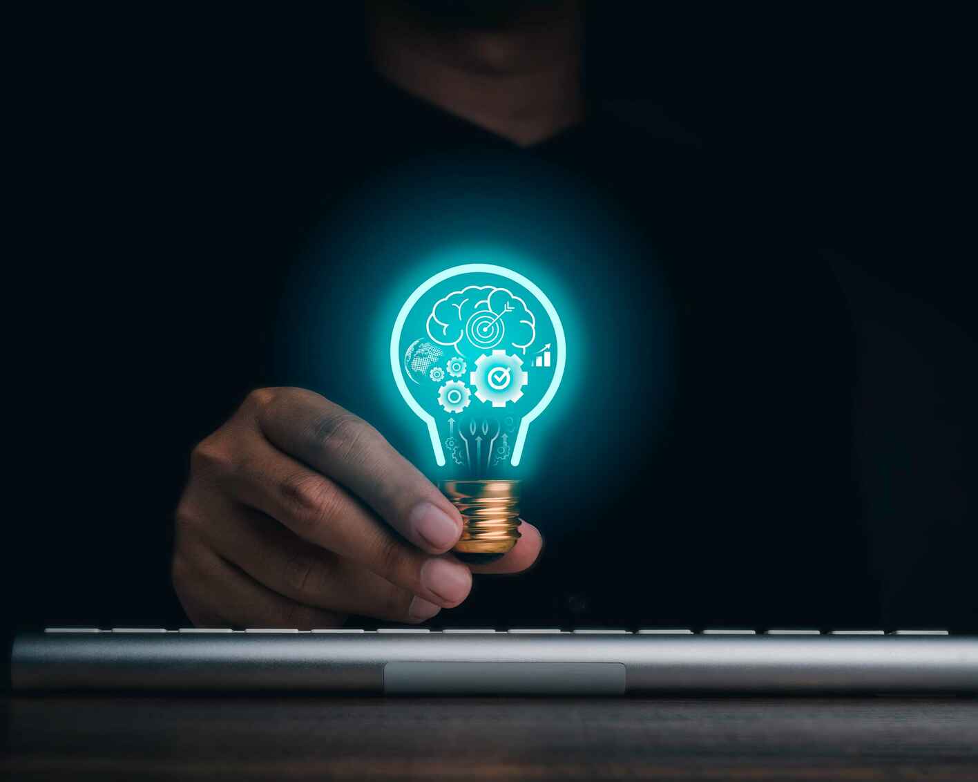 Photo of a man holding a light bulb over a keyboard, with graphics inside the light bulb such as gears and a brain