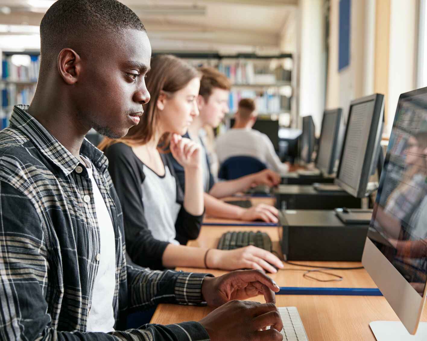 College students working on desktop computers in a library or classroom setting.