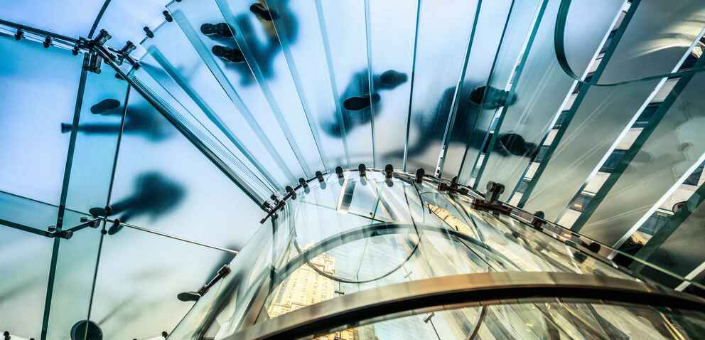 Looking up at glass stairs as people talk down them. The glass blurs the silhouette of the people. 