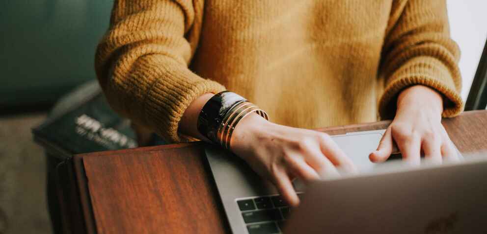 Student on laptop wearing a gold sweater.