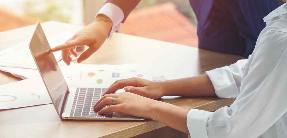 Businesswomen pointing at the laptop screen while her colleague/secretary is typing.
