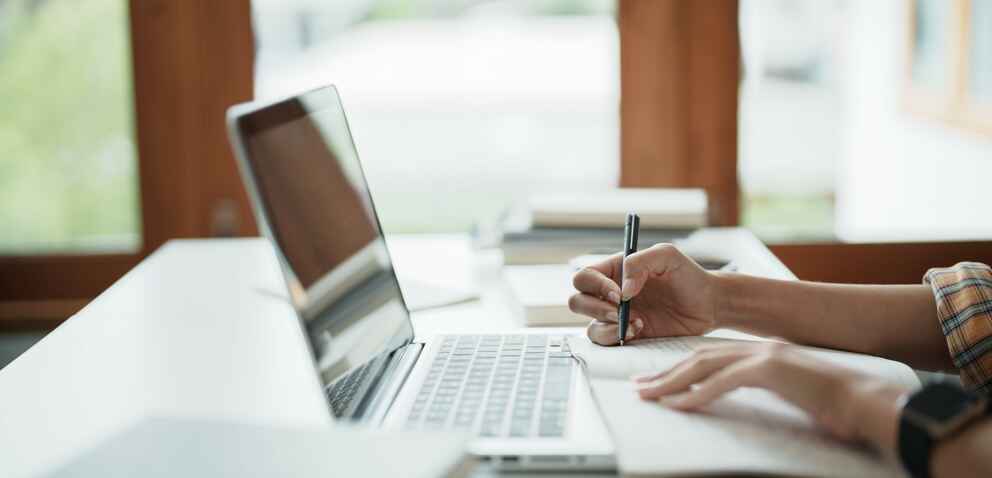 Young woman student busy studying make notes in notebook and using laptop.